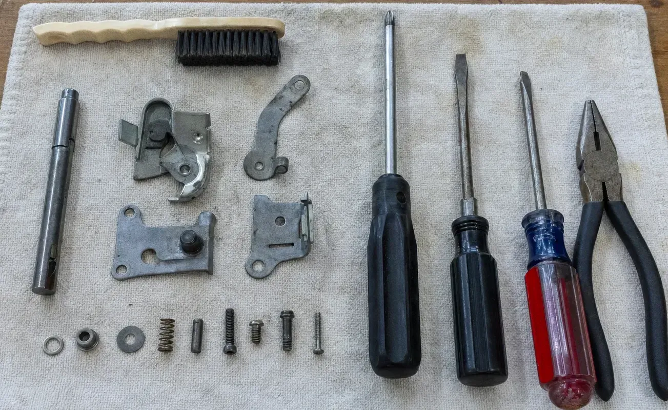 A wire brush, three screwdrivers, hinge plates, latch links, springs and loose screws arranged on a cloth